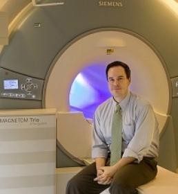 white man with brown hair sits on a the table of an MRI machine